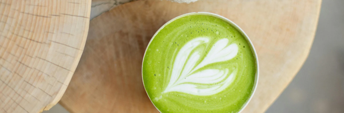 Latte de matcha avec un motif en feuille dessiné dans la mousse, servi dans une tasse en céramique posée sur un plateau en bois clair